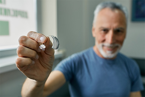 senior-man-holding-bte-hearing-aid-in-hand-on-foreground-close-up-treatment
